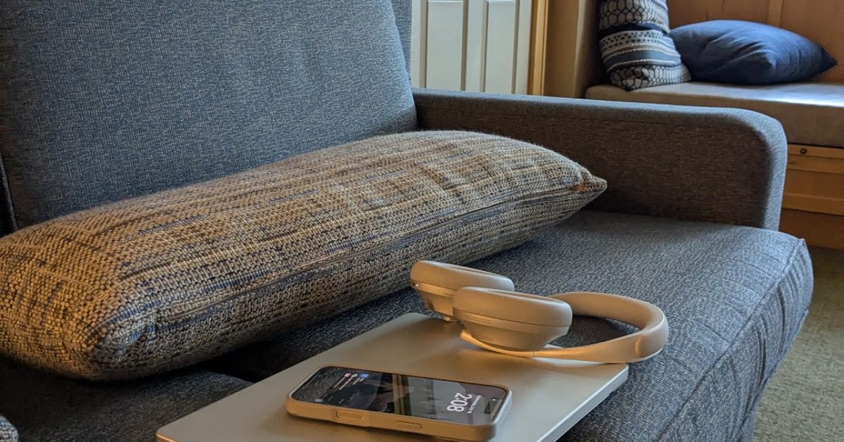 an iphone, macbook, and headphones on a couch